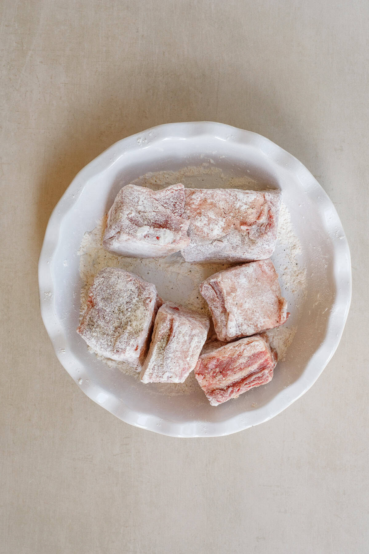 These slow cooker short ribs are made crispy in the dutch oven, and juicy and tender in the slow cooker. Seasoned and floured short ribs in a dish.