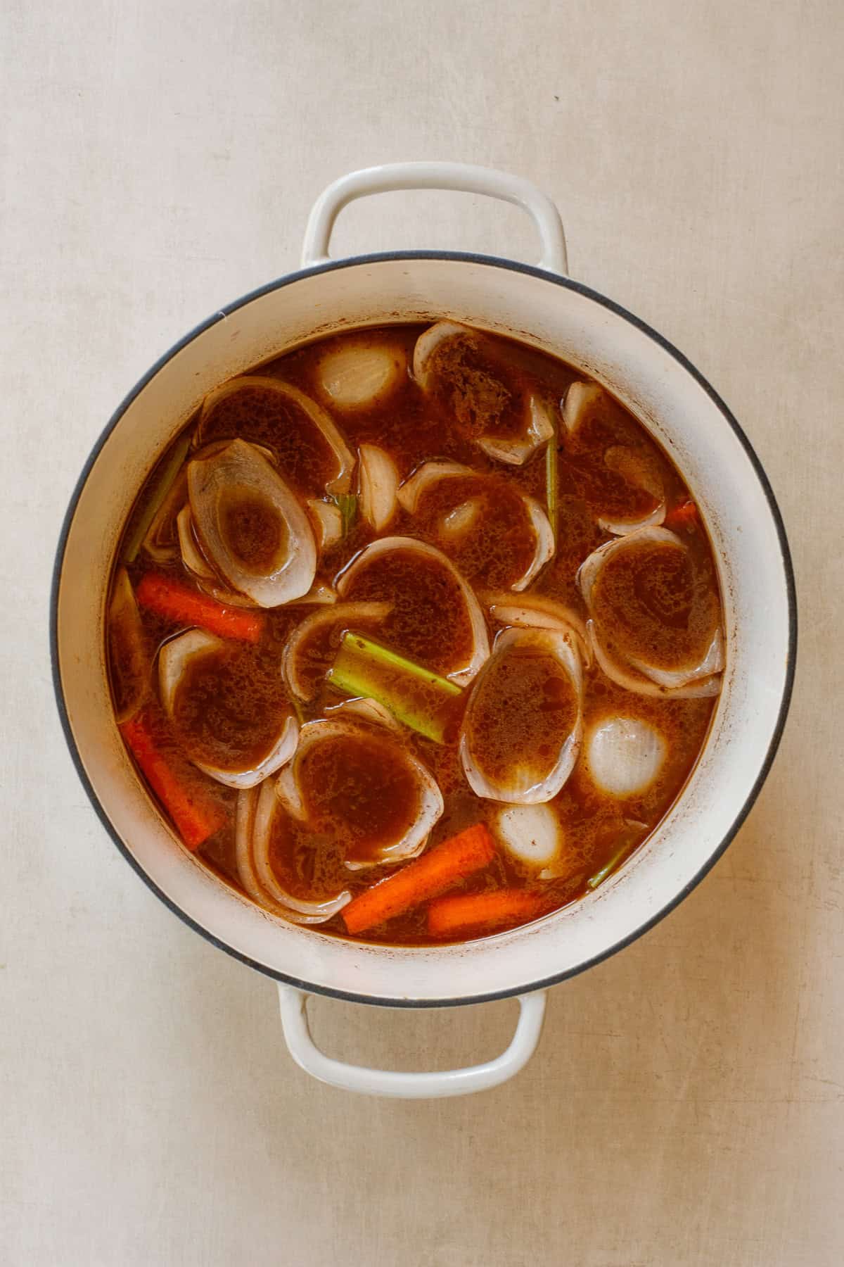 These short ribs slow cooker in a beef wine sauce and become so juicy and tender. A dutch oven with the vegetables and sauce cooking down.