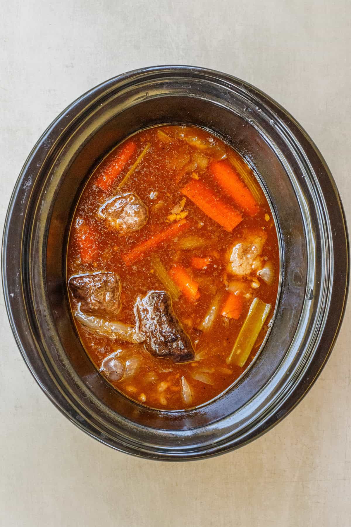 Our homemade slow cooker short ribs are so easy and delicious because the slow cooker did all the hard work. A slow cooker with the cooked short ribs in the sauce.