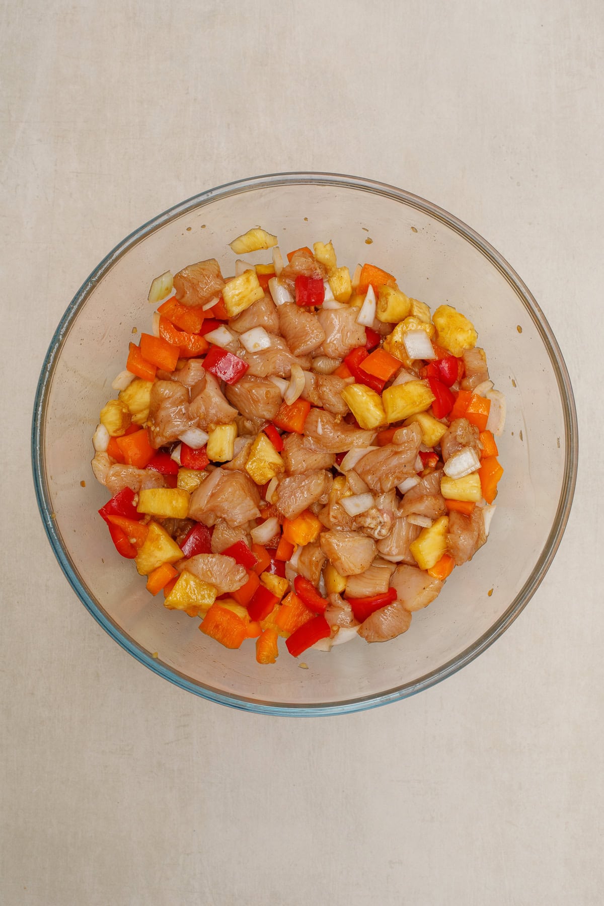 Our homemade hawaiian chicken sheet pan recipe is the go to for a quick and easy meal. A glass bowl with cubed chicken, veggies, and stir fry sauce.
