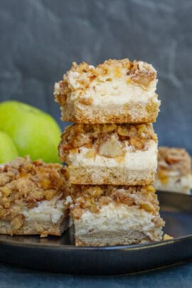 Loaded apple cheesecake bars are stacked on top of each other.