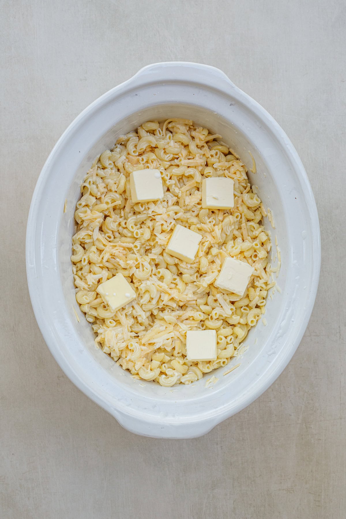 This classic mac and cheese is cooked to perfection in the slow cooker. This crockpot mac and cheese recipe makes the perfect comfort meal with little to no effort! A slow cooker with the ingredients for homemade mac and cheese, topped with butter.