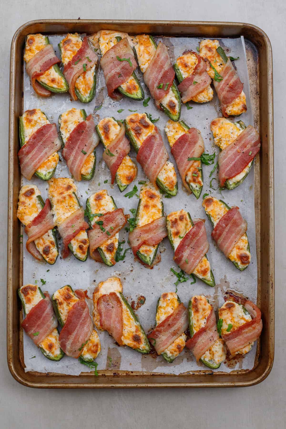 These cheesy jalapeno poppers are loaded with a cream cheese filling and baked until crispy in bacon. A baking sheet with the crispy bacon wrapped jalapenos.
