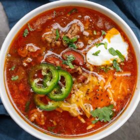 A bowl of crockpot chili topped with fresh jalapeno slices, cheddar cheese, and sour cream.