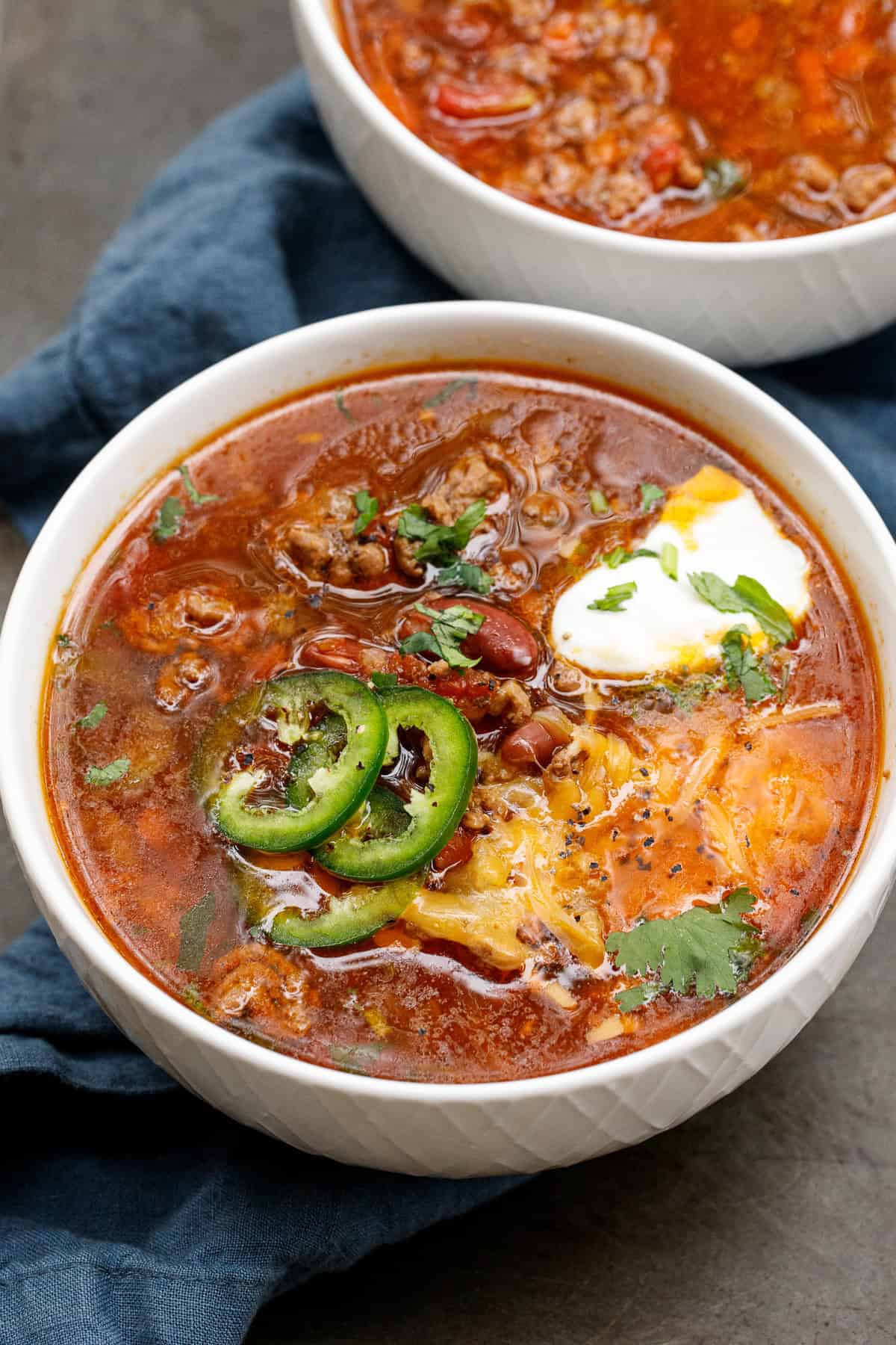 Each bowl of crockpot chili is topped with fresh jalapneos, sour cream, and cheese. A bowl of slow cooker chili topped with jalapenos, sour cream, and cheese.
