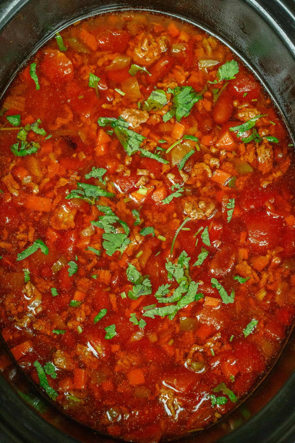 This homemade chili recipe is the perfect slow cooker recipe. A crockpot with the cooked chili, garnished with fresh herbs.