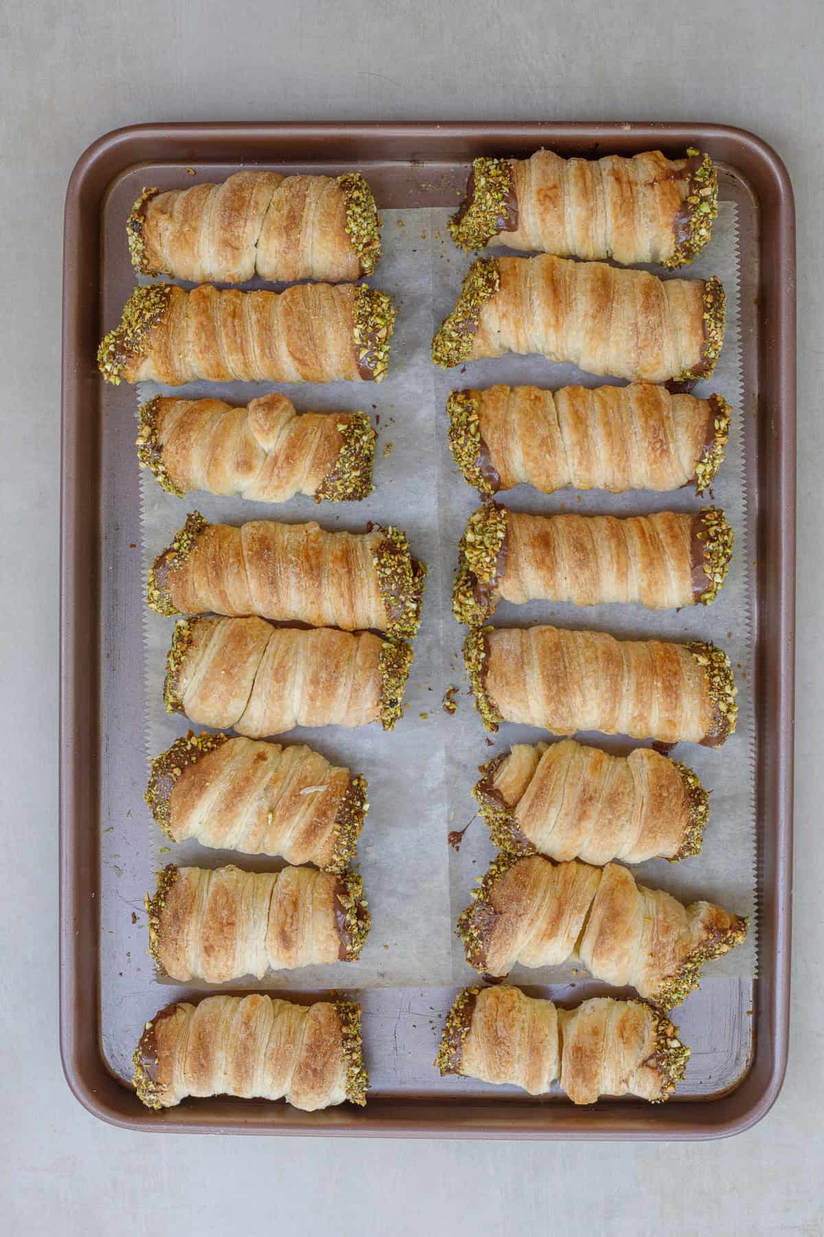 These crispy dubai chocolate horns are the perfect holiday dessert to make from scratch. A baking sheet with the chocolate coated horns filled with pistachio buttercream.