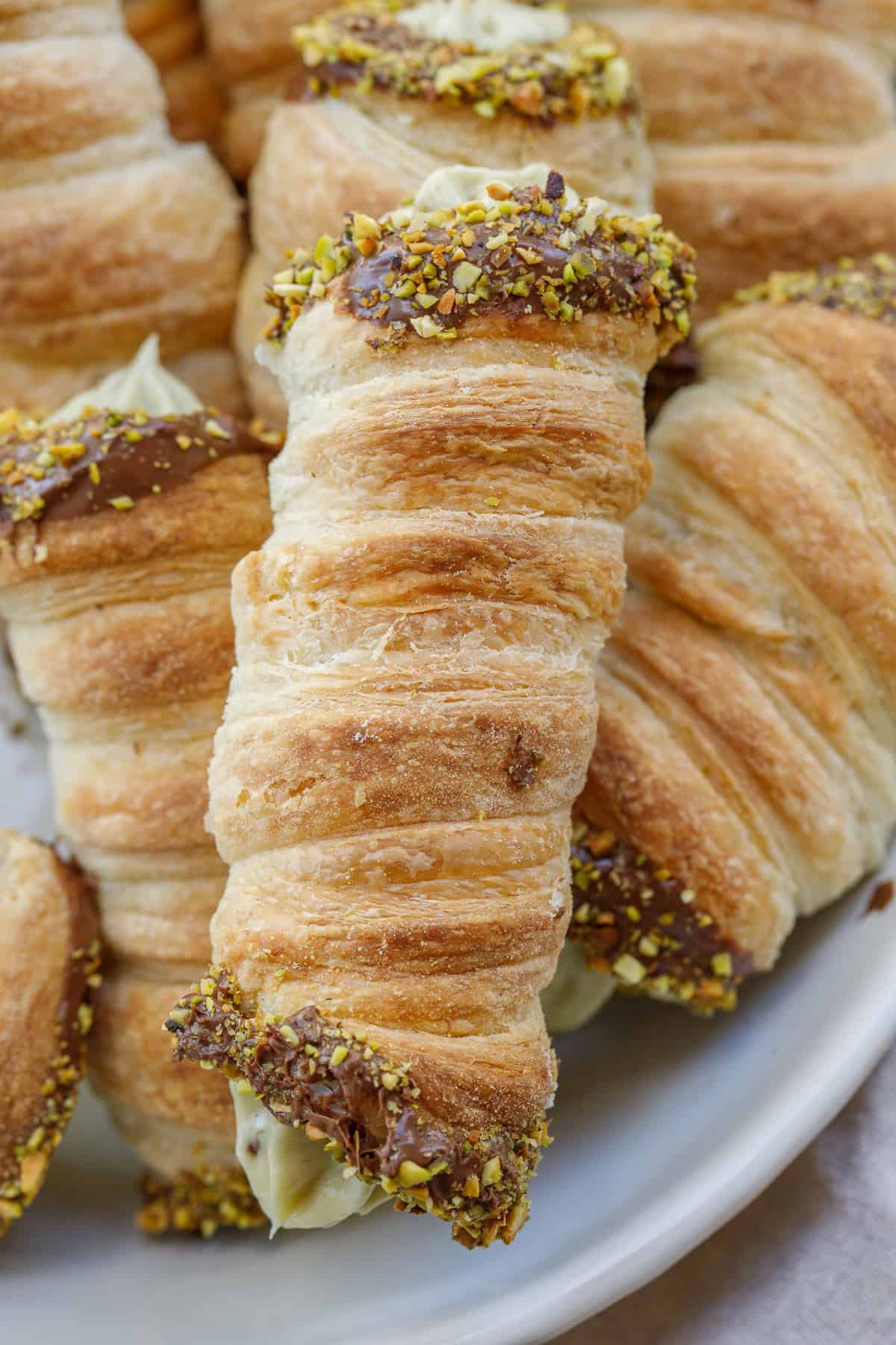 These dubai chocolate cream horns are made with a crisp puff pastry, a rich pistachio buttercream, and a chocolate pistachio coating. A golden brown puff pastry horn filled with pistachio buttercream.