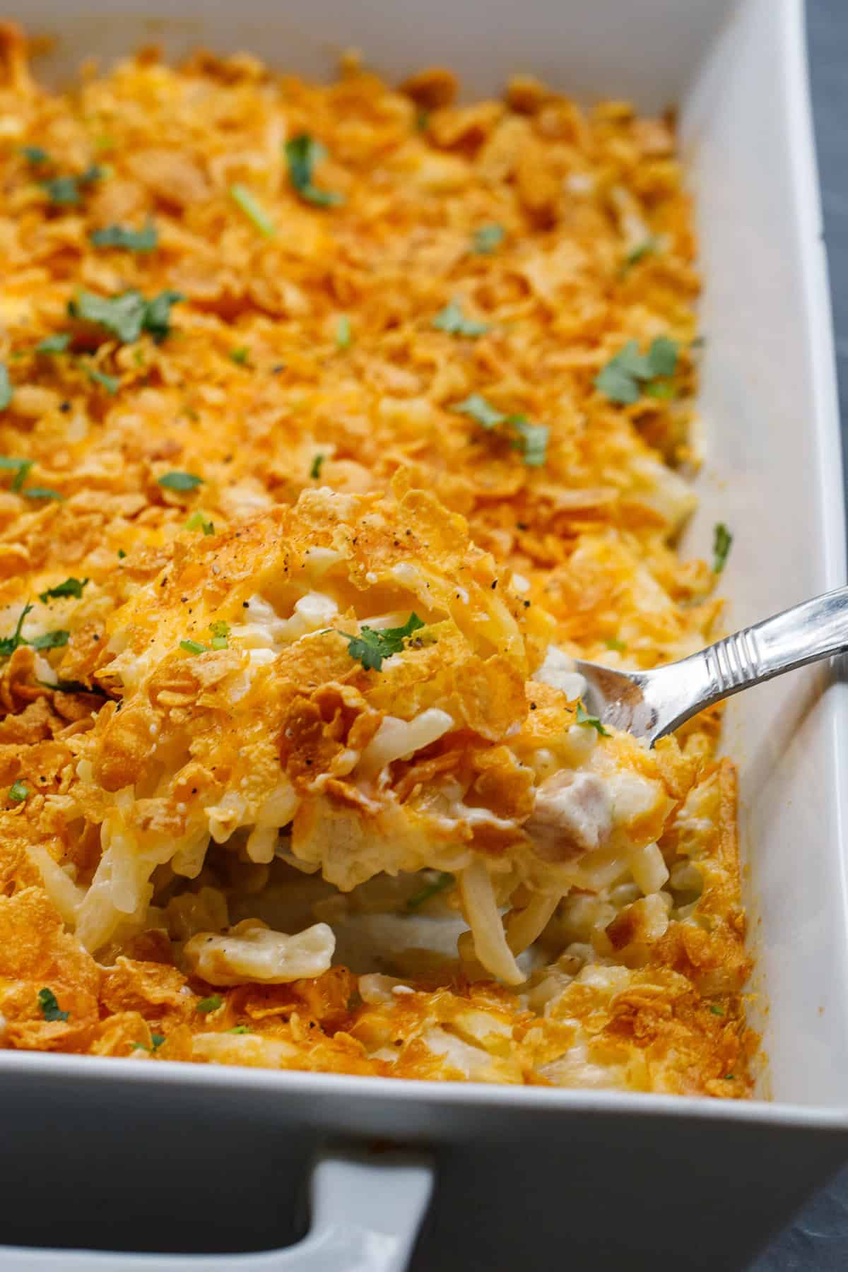 A cheesy hash brown casserole, perfect for a crowd, or as a holiday side. A casserole dish with a spoonful of cheesy hashbrown.
