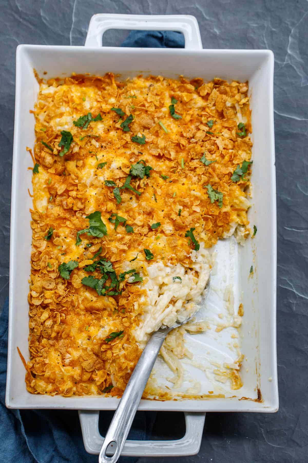 This classic hash brown recipe is made unforgettable with a topping of shredded cheese and crisp corn flakes. A casserole dish with spoonfuls of hash brown casserole.