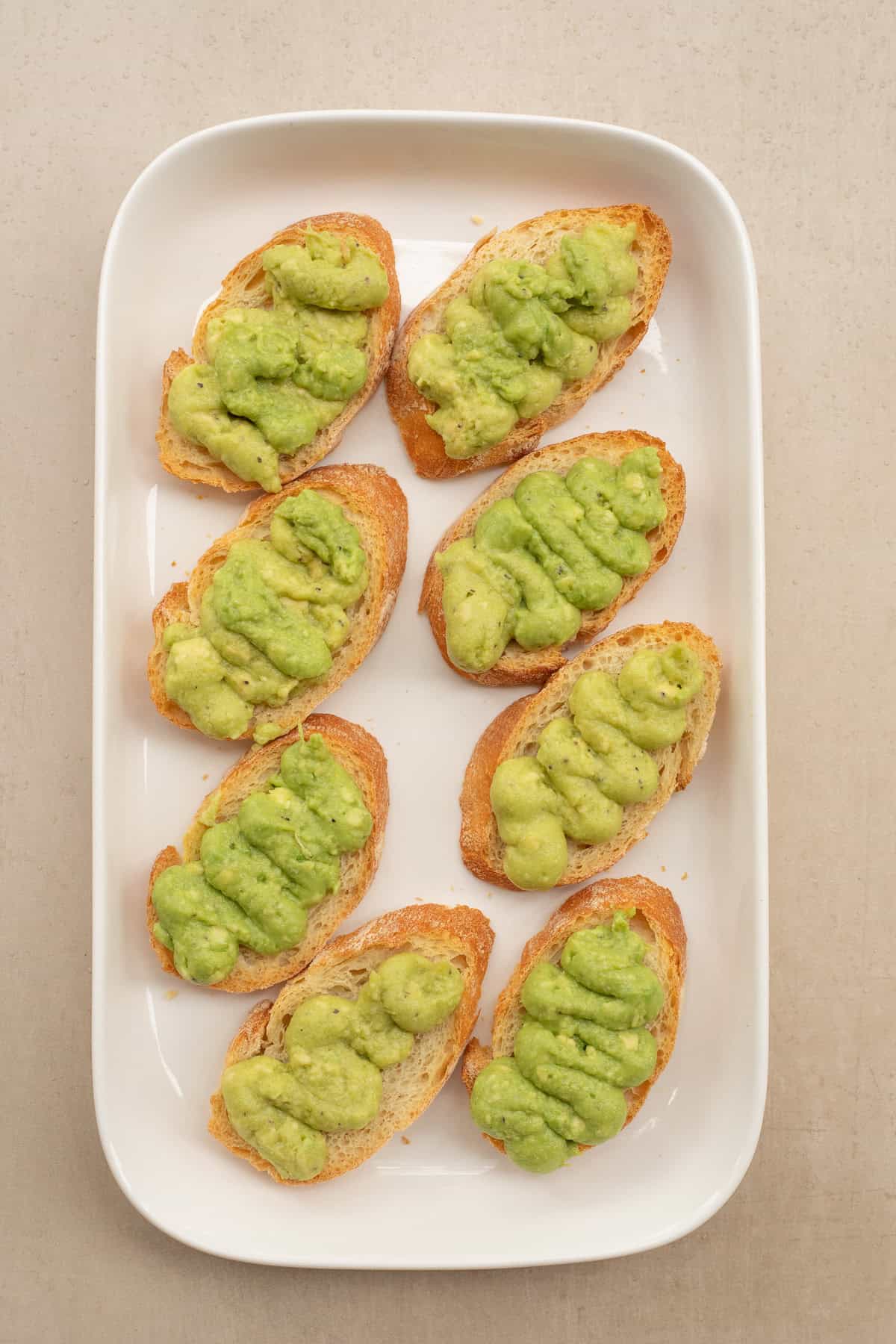 A shrimp and avocado open faced sandwich recipe. A white tray with the bread slices and a piping of the avocado cream.