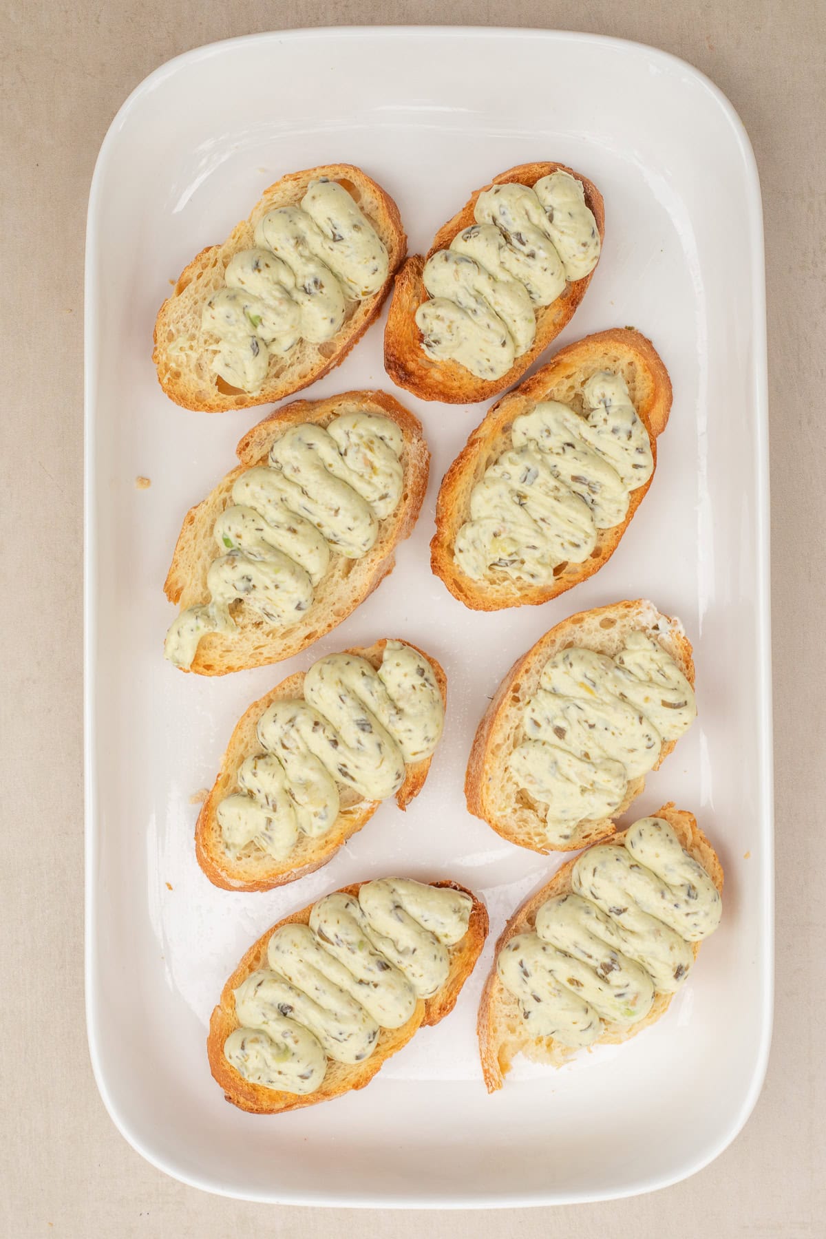These quick pesto and tomato canapes make the perfect finger food. A tray withe the crispy bread and and creamy pesto piped onto each slice.