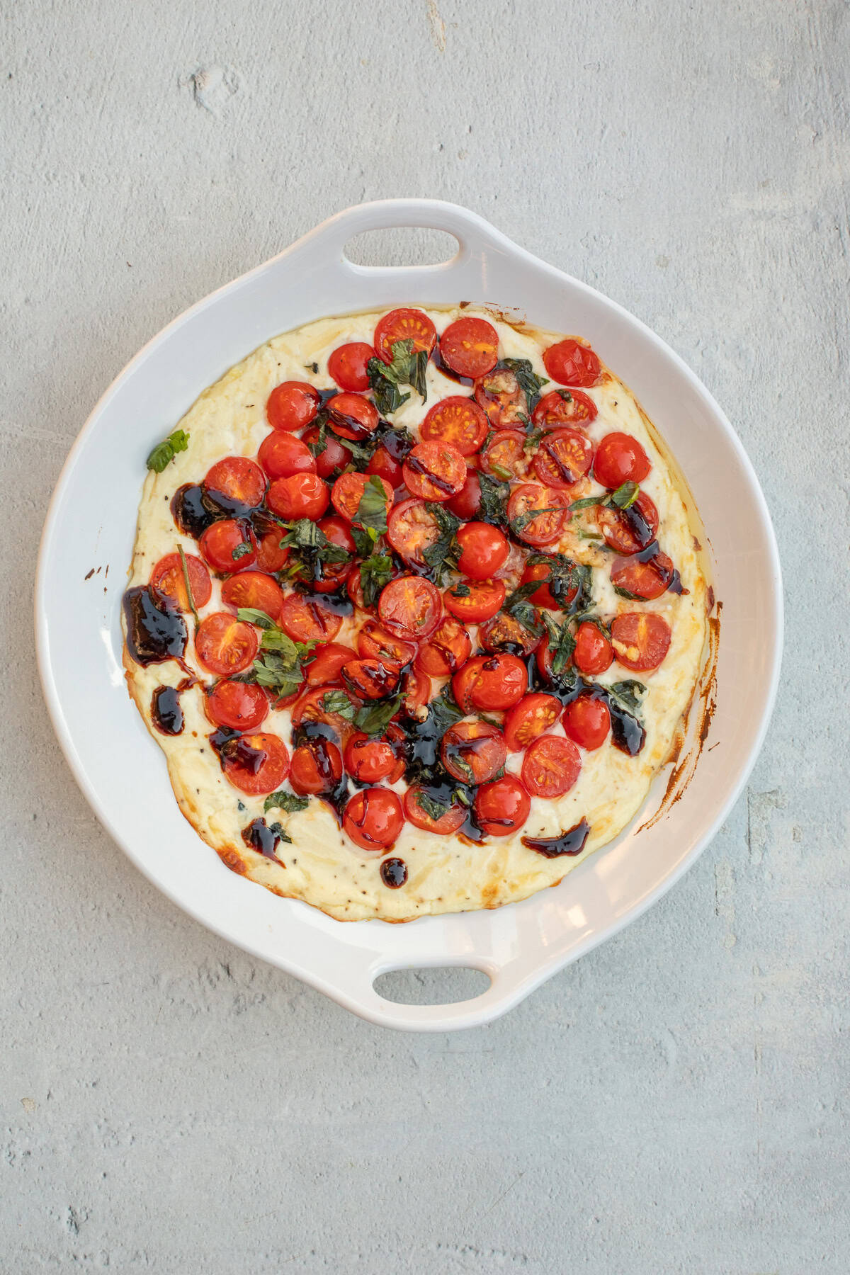 Rich and creamy ricotta cheese dip, topped with a roasted tomato mix. A baking dish with the baked ricotta and tomato dip.