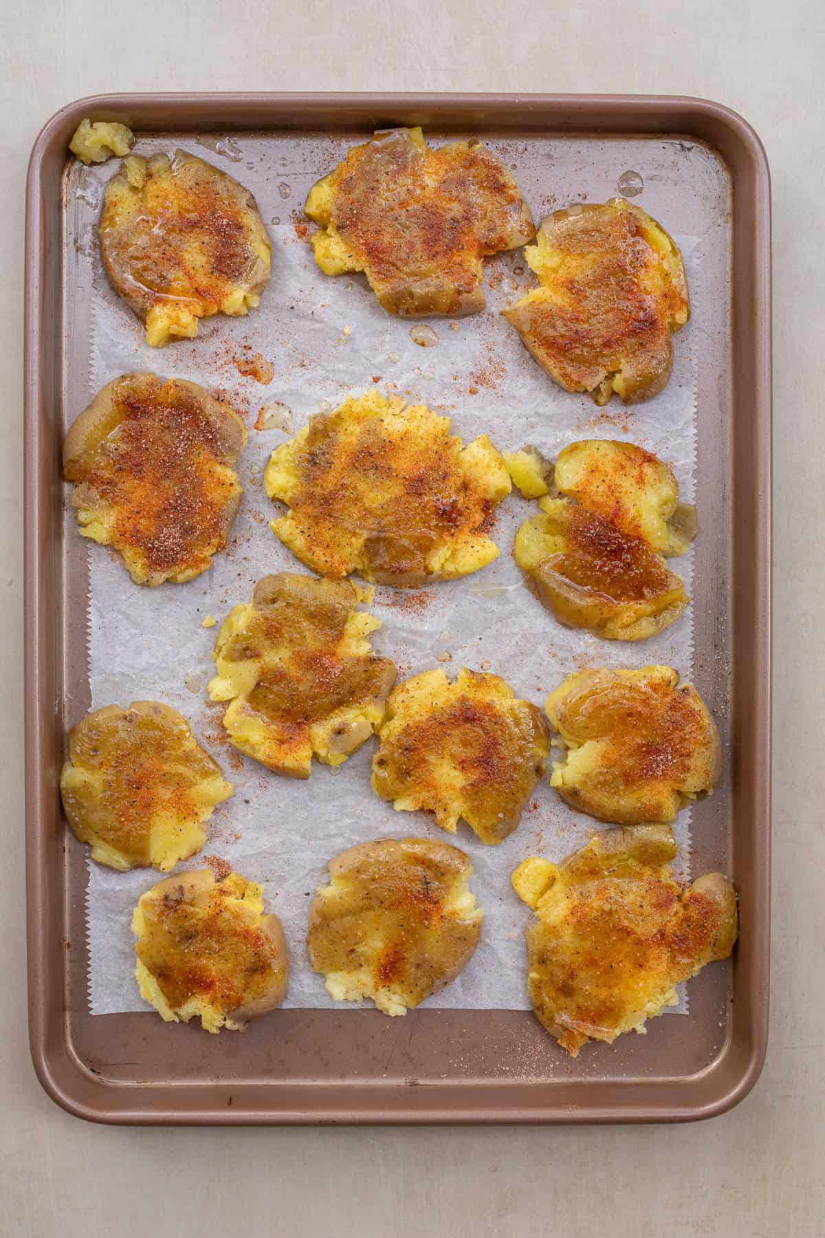Crispy Smashed Potatoes for Holidays. A baking sheet with the smashed potatoes, seasoned with oil and seasoning.