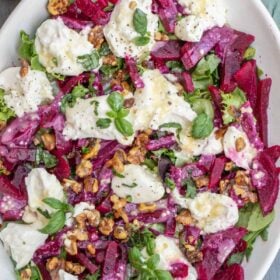 A white plate with the beet burrata salad topped with walnuts.