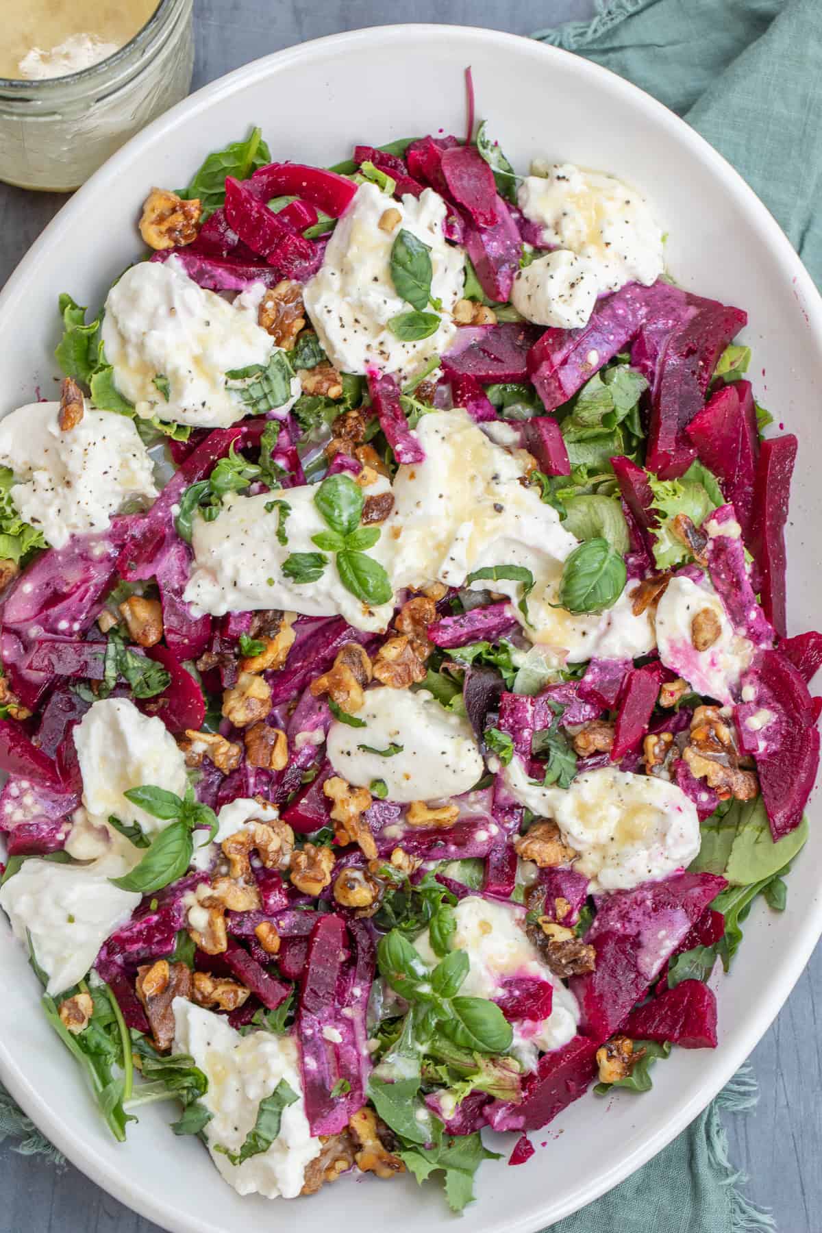 A white plate with the beet burrata salad topped with walnuts.