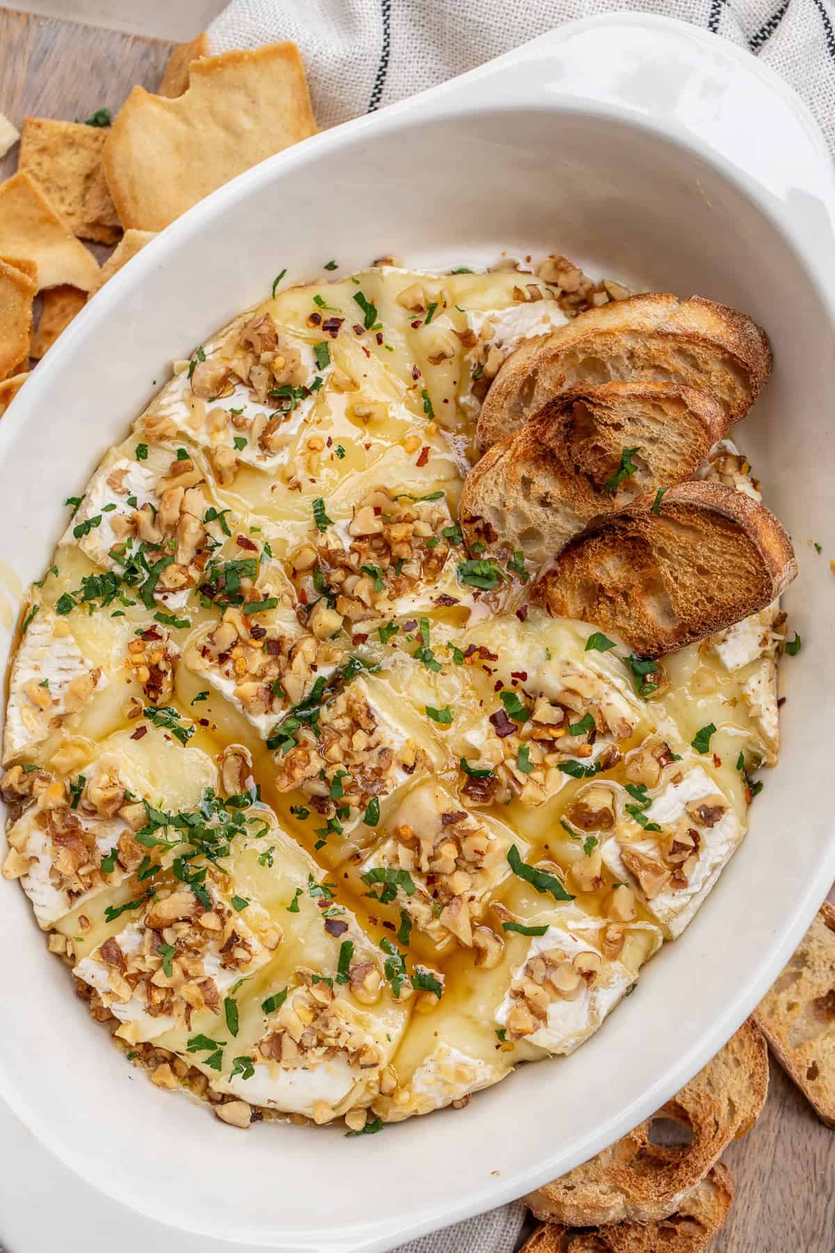 Serve a homemade baked brie with baguette slices, crackers, and pita chips. A casserole dish with baked brie, served with sliced toast.