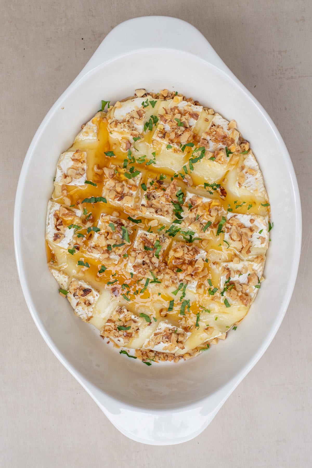 A simple appetizer: baked brie cheese from scratch. The casserole dish with the baked brie, topped with honey and fresh herbs.