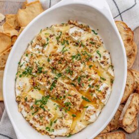 A serving dish with baked brie, topped with honey and herbs.