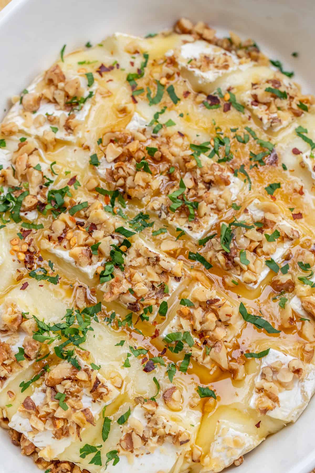 A melty baked brie cheese topped with crispy walnuts, honey, and fresh herbs. The perfect appetizer to serve for a crowd. A baked brie topped with walnuts, fresh herbs, and honey.