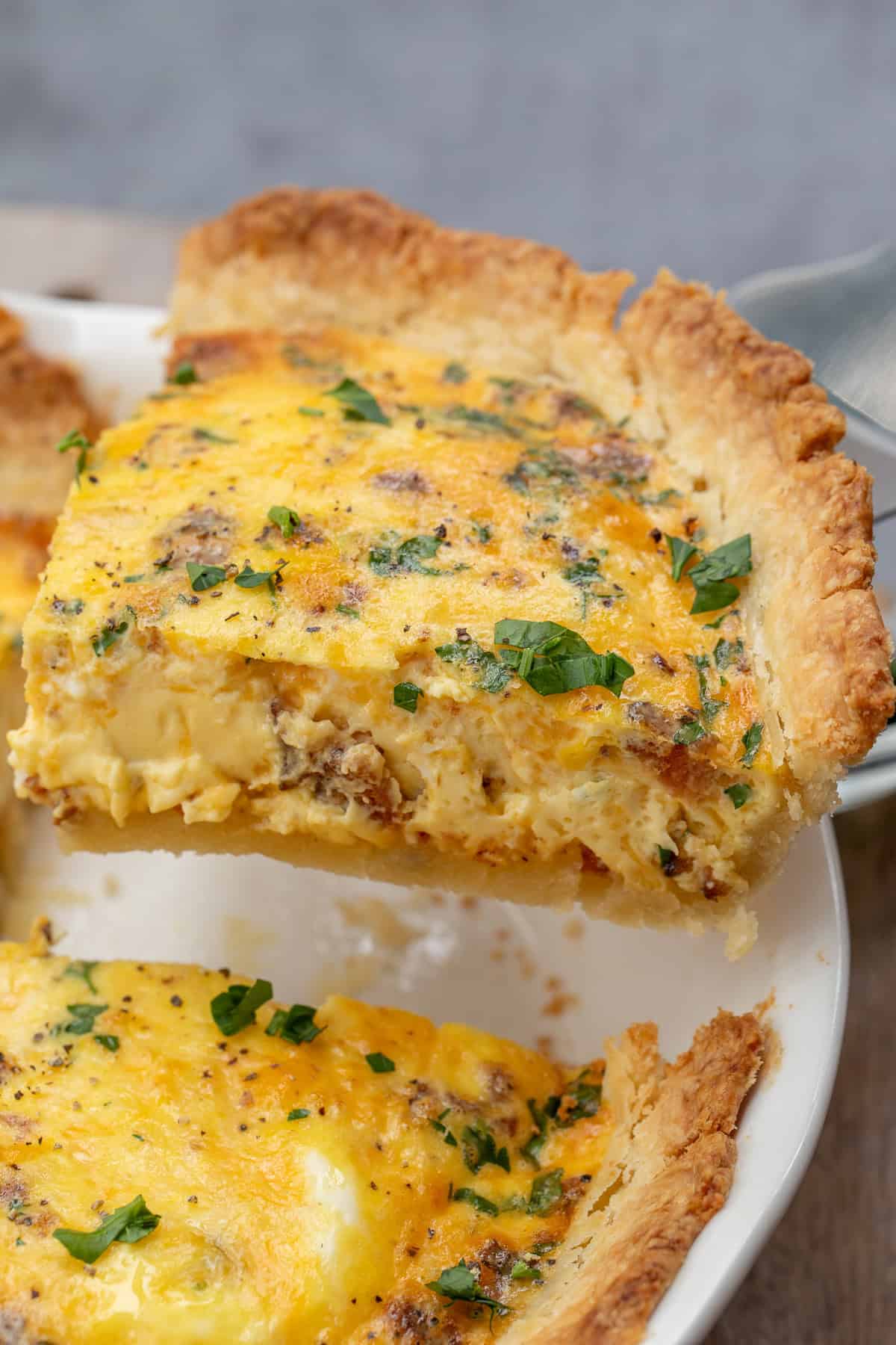 This baked quiche recipe makes the perfect homemade quiche from scratch. A simple pie crust, loaded with a delicious egg filling. A slice of baked quiche, topped with fresh herbs.