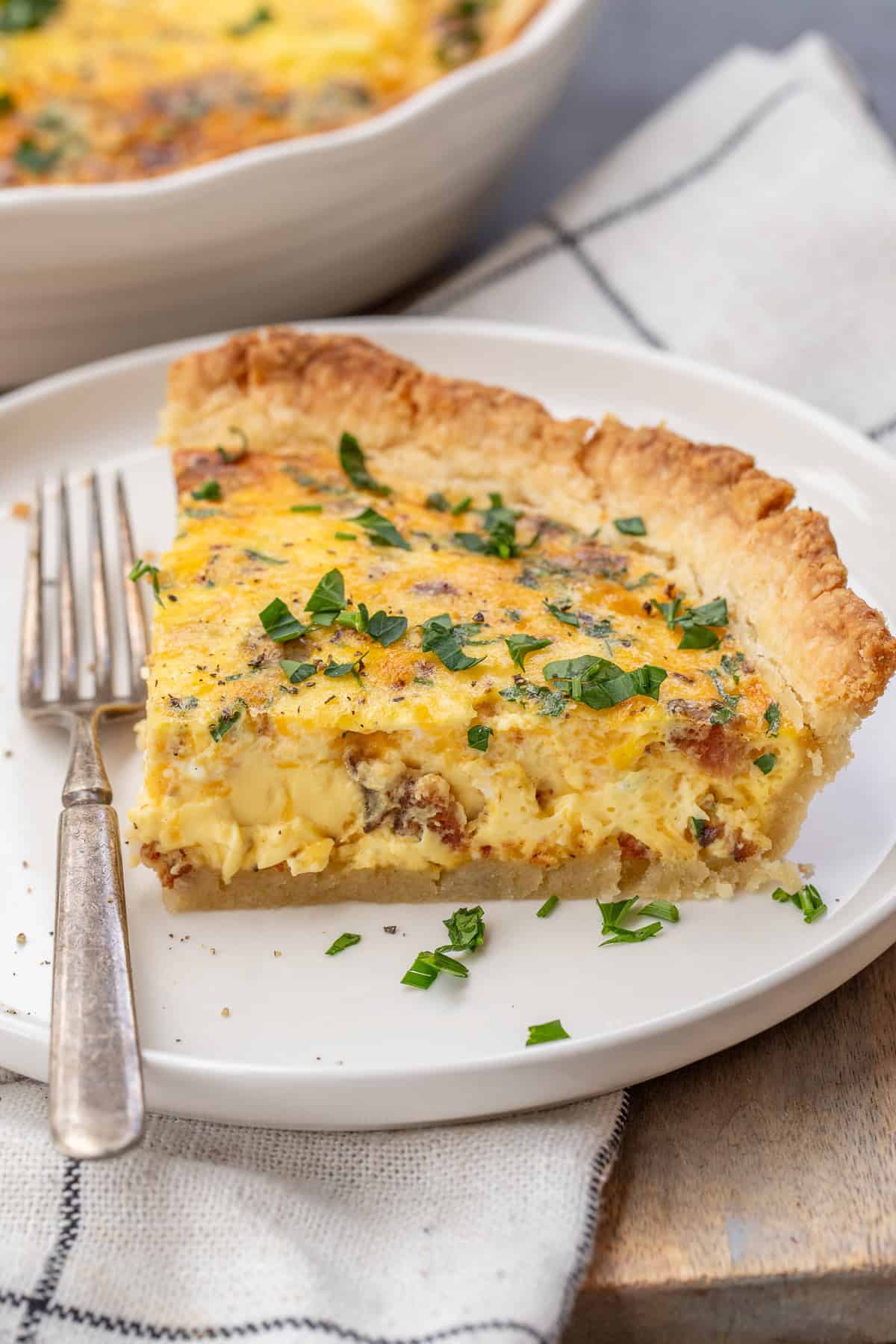 This easy quiche recipe consists of a homemade pie crust, filled with a silky egg filling. A plate with a slice of baked quiche.