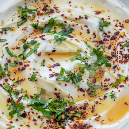A bowl with the ricotta spread, topped with honey, fresh herbs, and red pepper flakes.