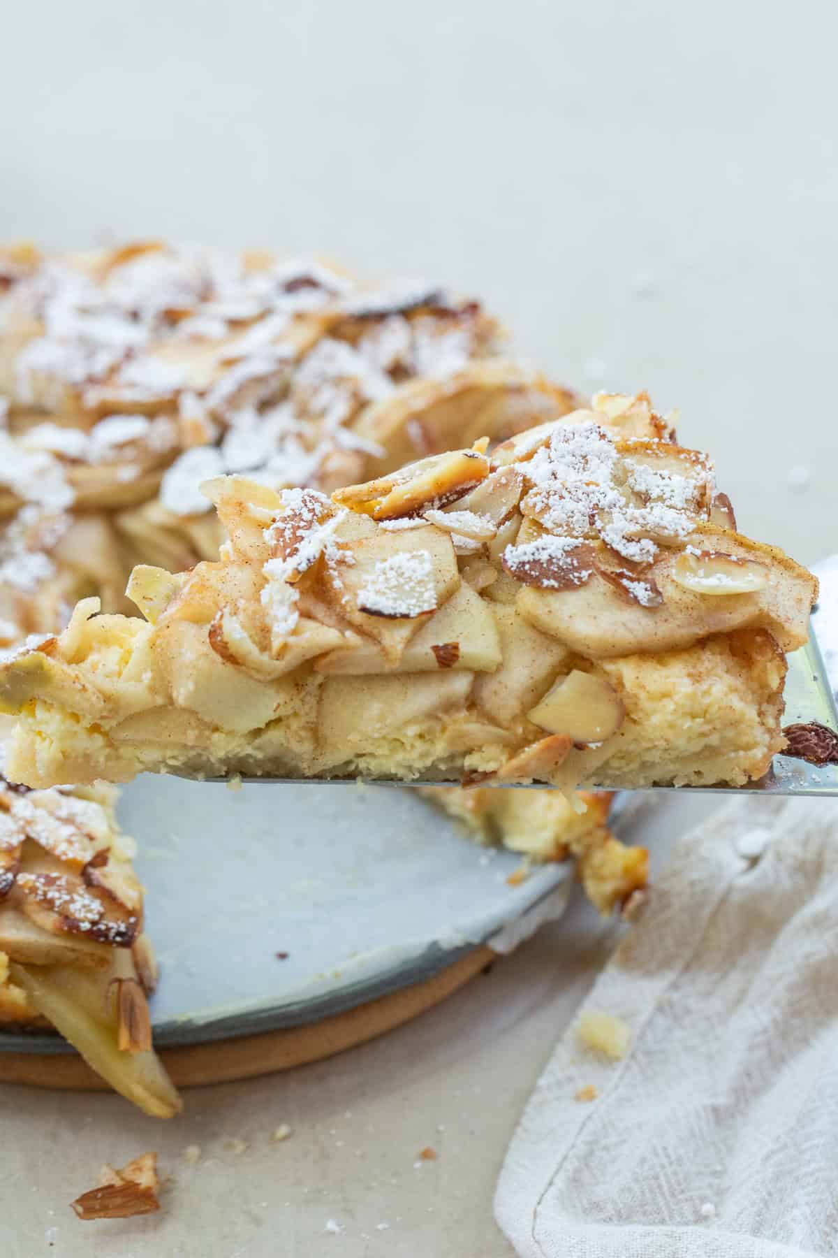 A classic Bavarian apple torte recipe made with sweet apples, rich cream cheese filling, and sliced almonds for the perfect balance of flavor and texture. This easy dessert looks impressive but is surprisingly simple to make. A slice of apple torte topped with powdered sugar.