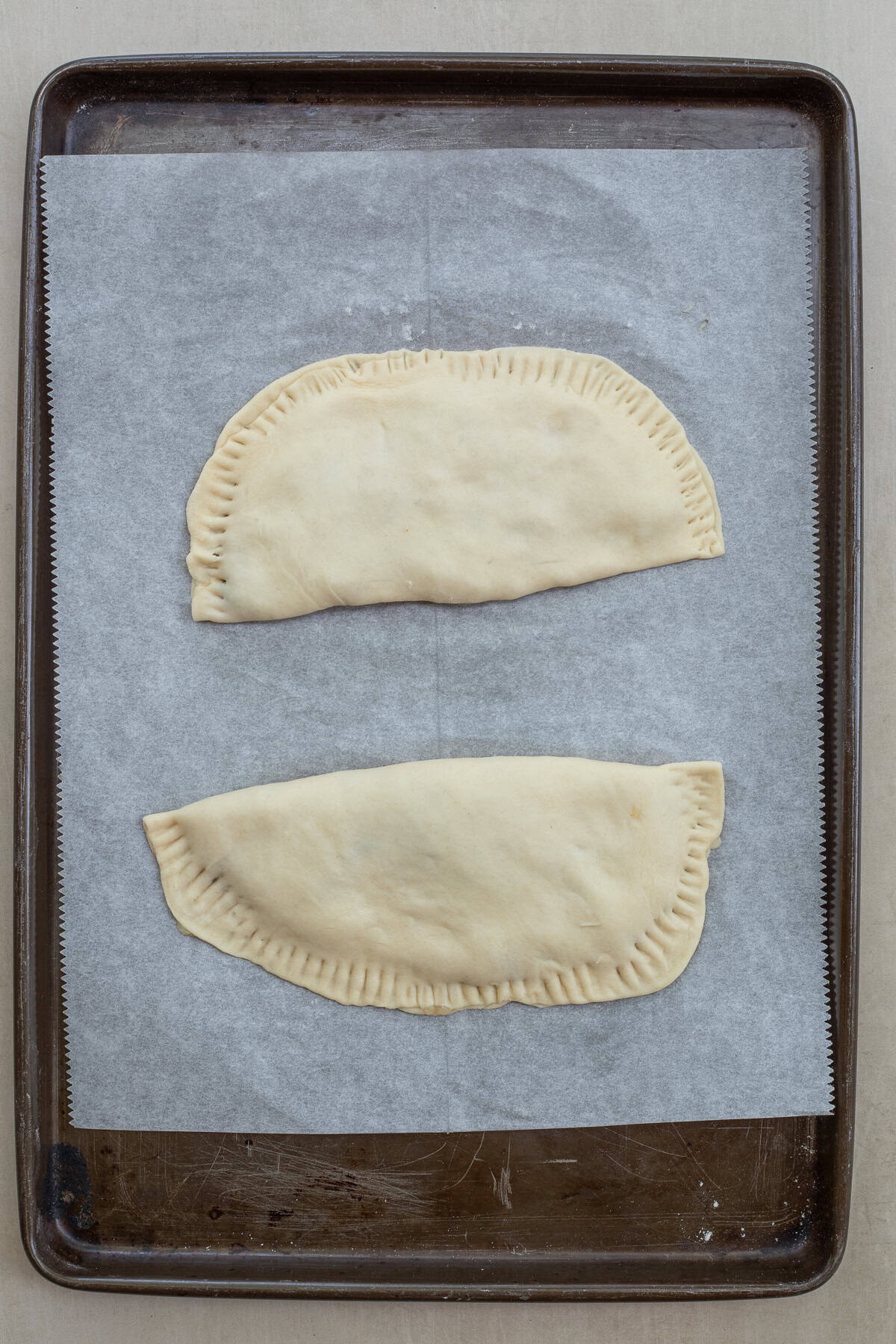 A chicken chebureki entree made from scratch. A baking sheet with the assembled chebureki.