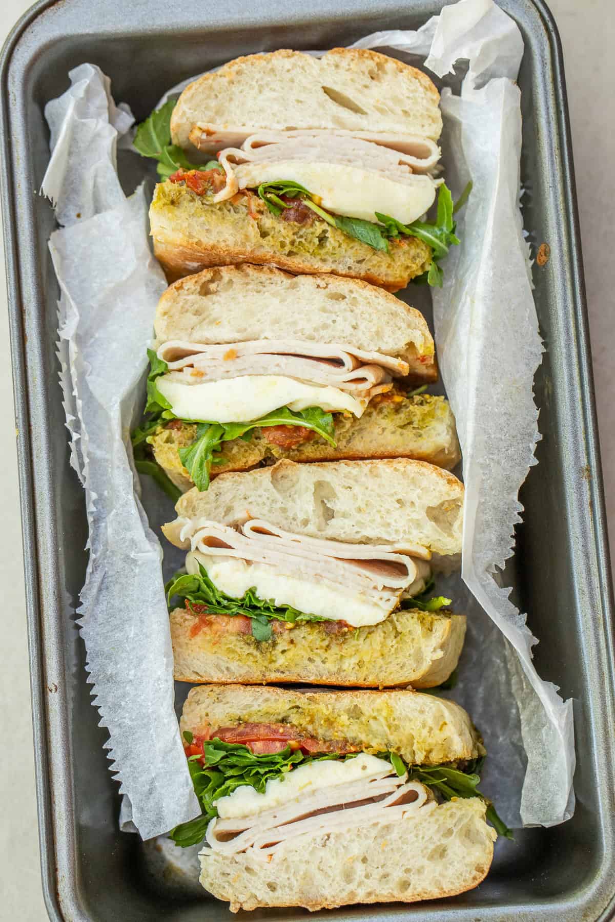 Best Chicken Pesto Sandwich Recipe Cut chicken pesto sandwiches showing the layers of chicken, cheese, and tomatoes.