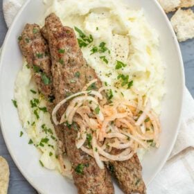 A plate of mashed potatoes with ground lamb kebabs.