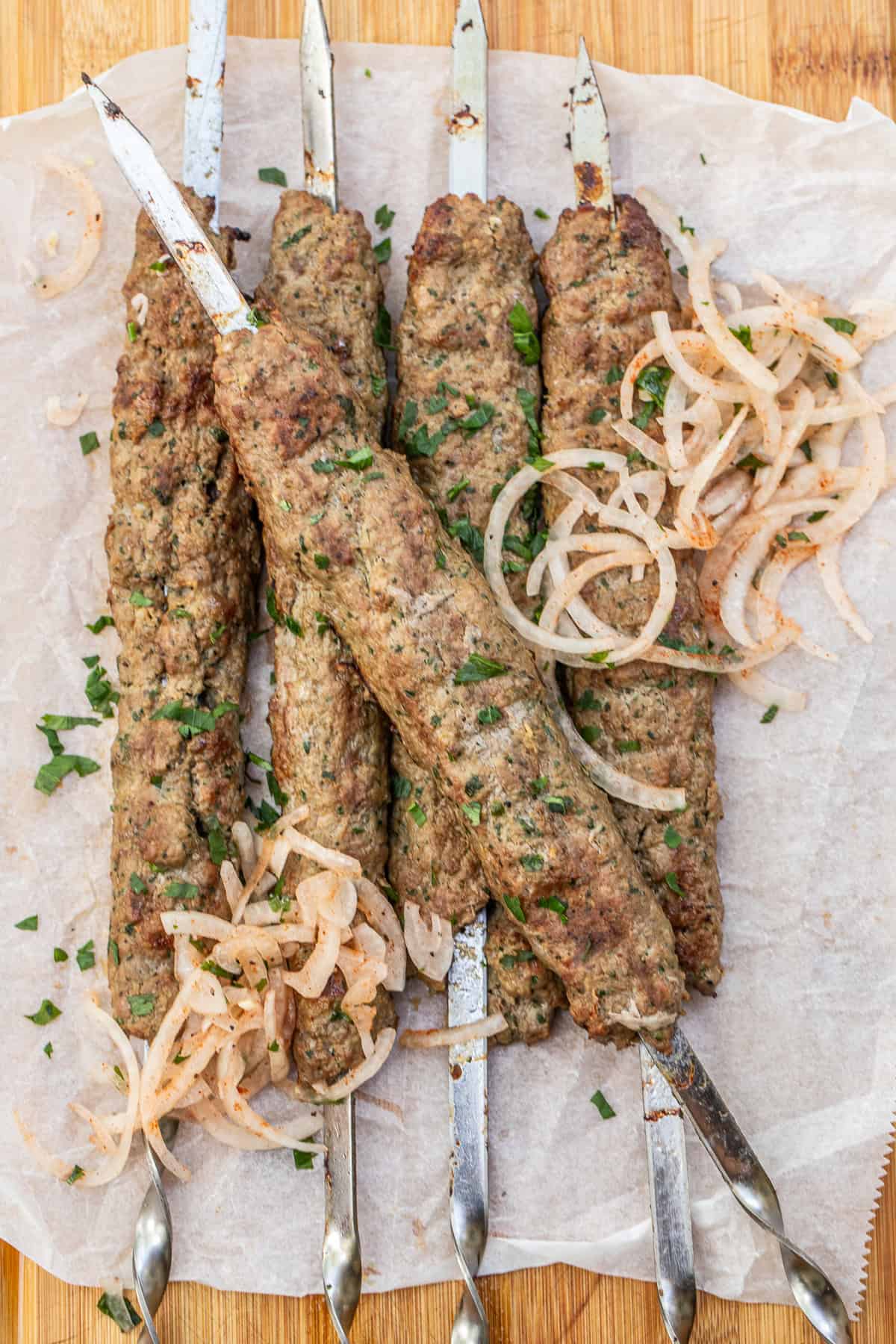 Ground Lamb Kofta Kebabs with Fresh Herbs and Spices A cutting board with the grilled lamb kebabs topped with onion salad.