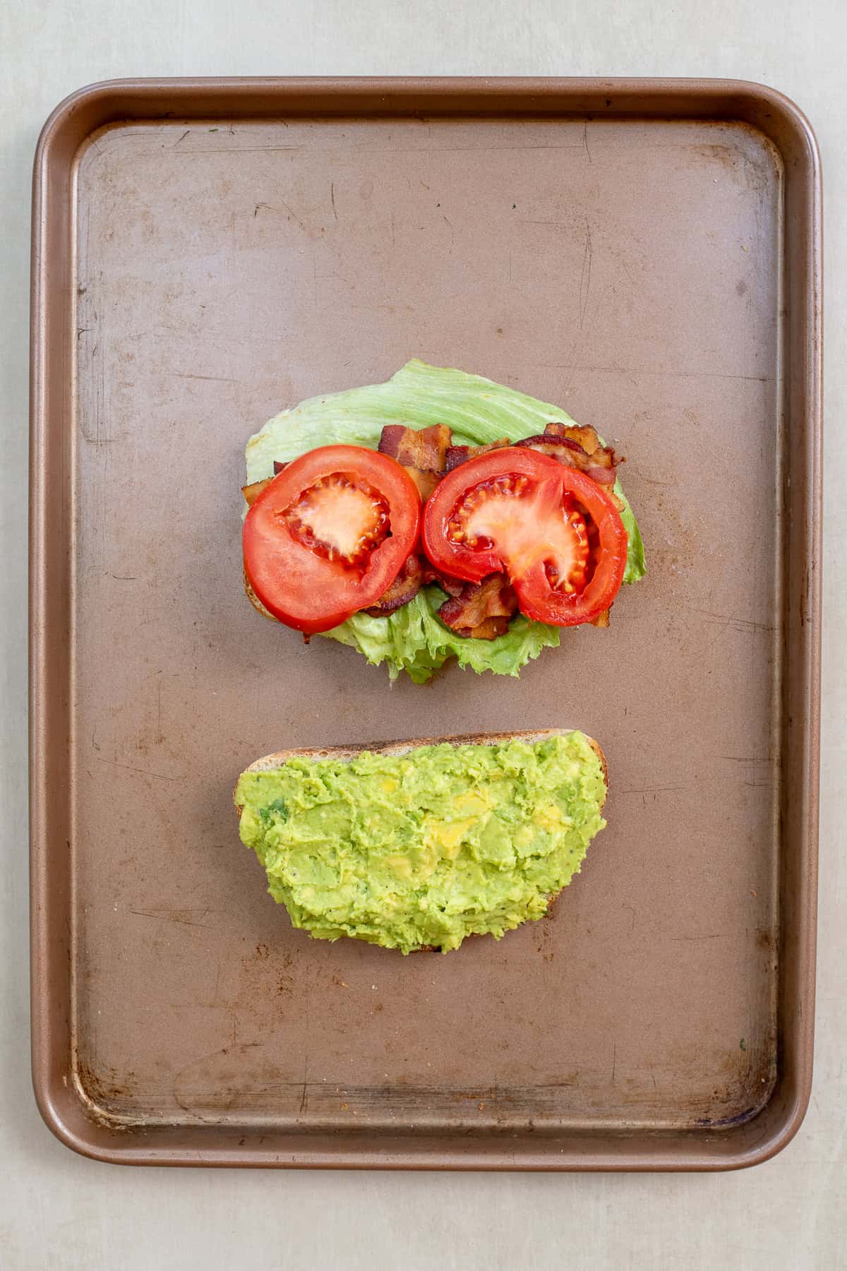 This easy BLT sandwich recipe comes together in minutes with fresh, flavorful ingredients. The blt sandwich being assembled with one slice of bread with avocado sauce, and the rest of the toppings on the other slice.