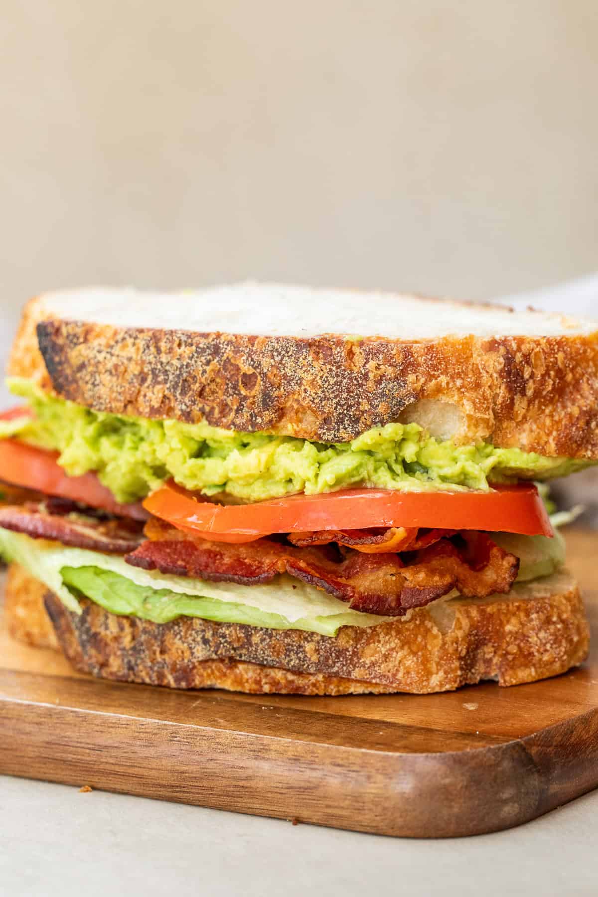 A layered blt sandwich showing avocado spread, tomatoes, bacon, and lettuce.