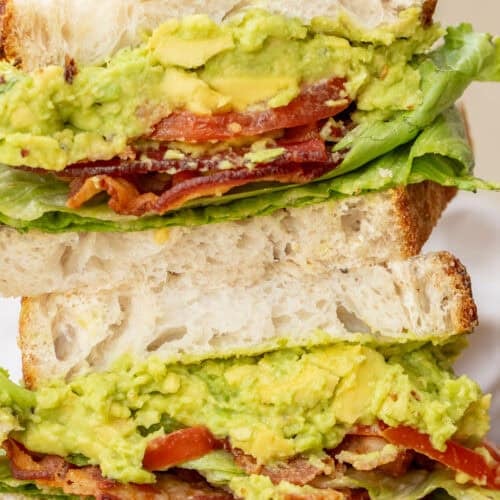 A stacked blt sandwich showing the layers of creamy avocado spread, crispy bacon, and juicy tomatoes.