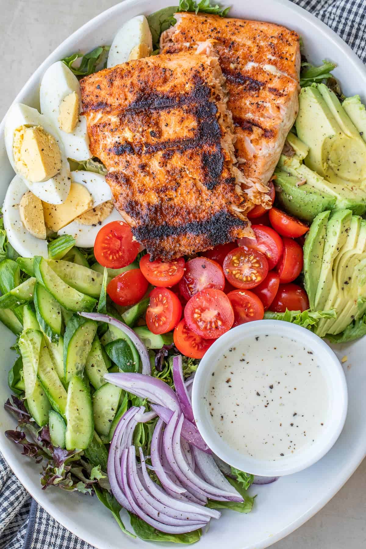 This healthy grilled salmon salad is loaded with fresh vegetables, flaky salmon, and a flavorful dressing. A large salad bowl with grilled salmon and salad.
