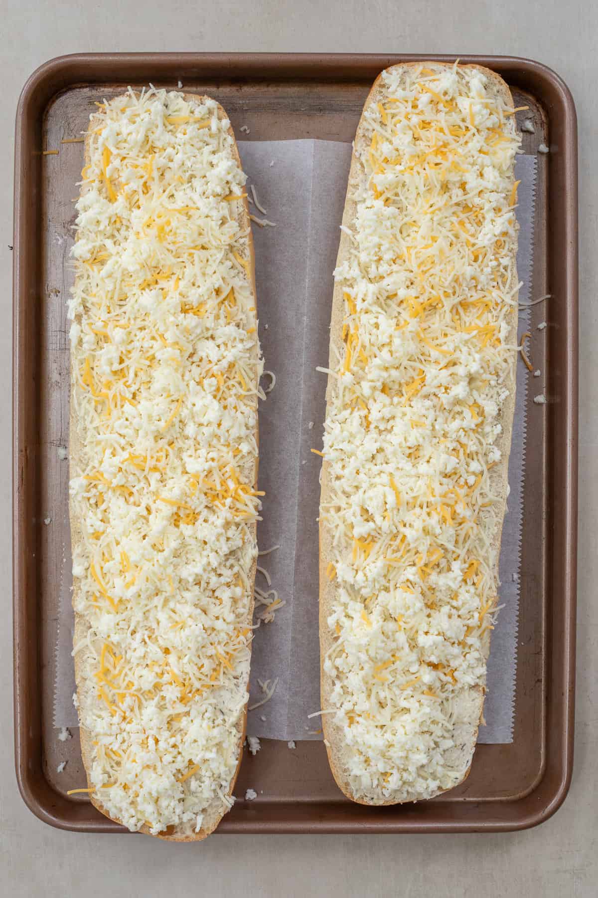 How to Make the Best Garlic Cheesy Bread at Home A baking sheet with the loaves of bread topped with cheese.