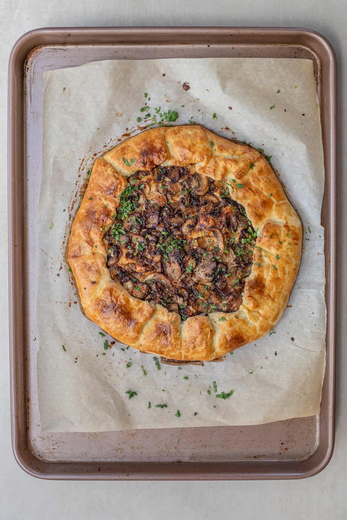 This homemade mushroom galette combines sautéed mushrooms, herbs, and cheese in a flaky pastry dough. The baked cheesy mushroom galette.