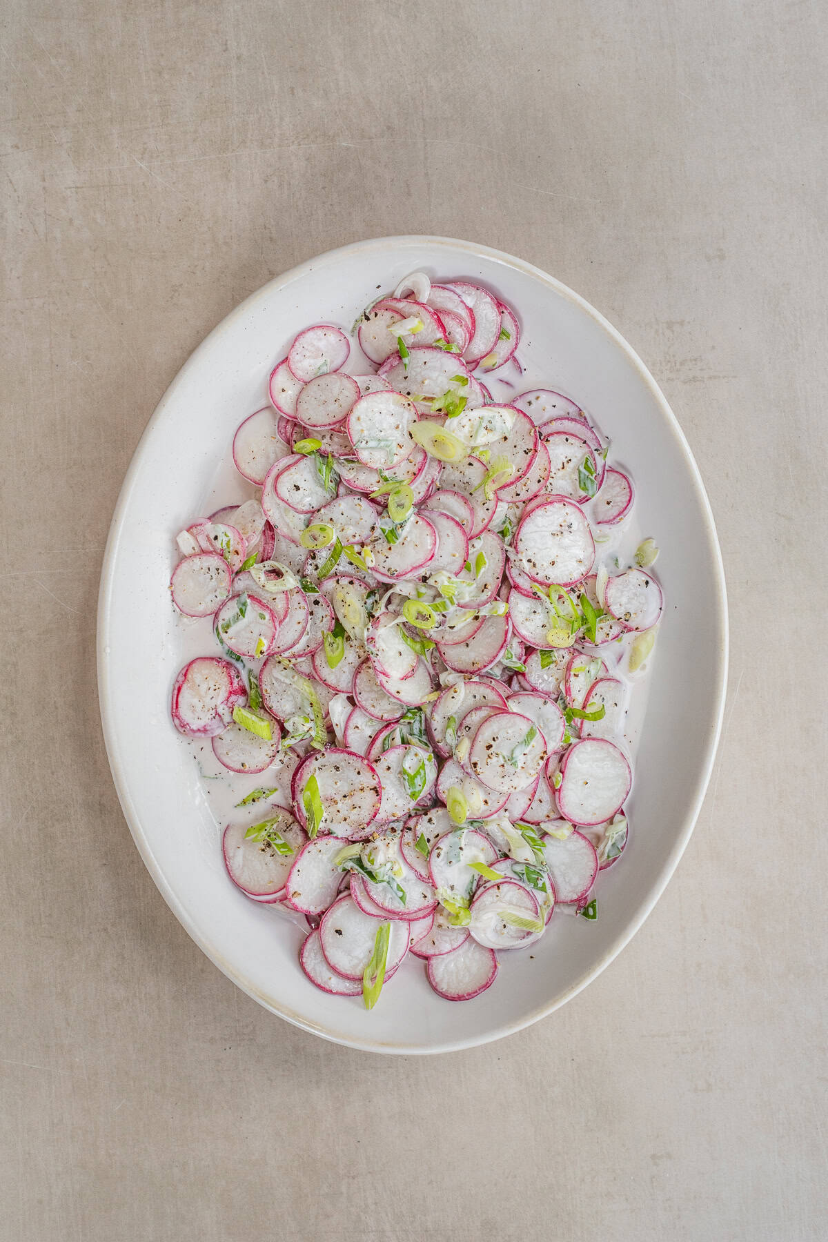 Thinly sliced radishes are tossed together to make a fresh salad. A salad bowl with a creamy radish salad.
