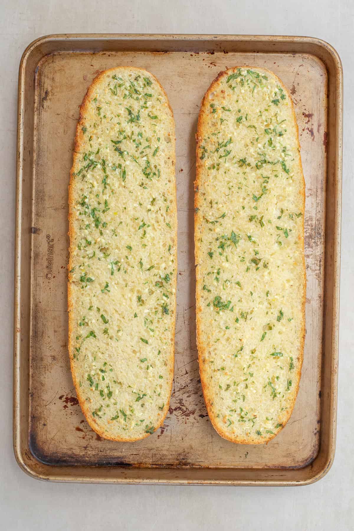 Slices of homemade garlic bread are perfect for dipping into pasta sauce. A baking sheet with the baked garlic bread loaves.