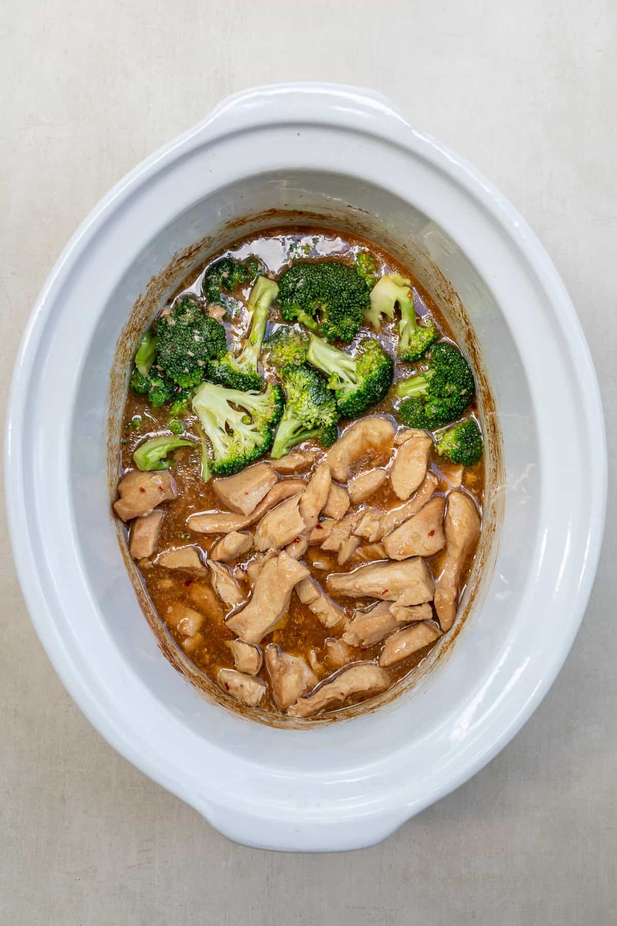 Easy crockpot teriyaki chicken served over rice for a simple and flavorful family dinner. A crockpot with the cooking chicken and broccoli.