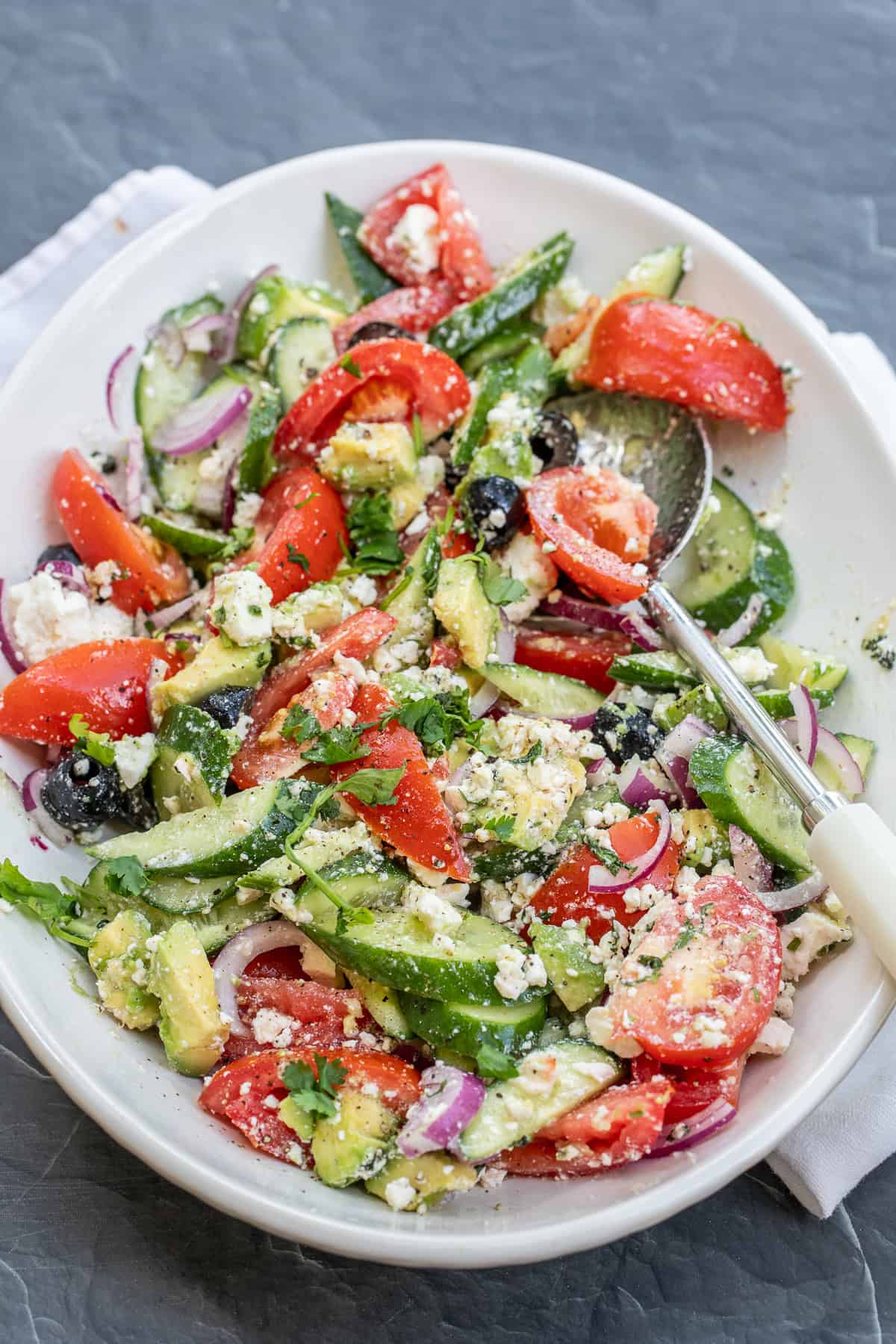 Easy avocado Greek salad loaded with fresh vegetables, creamy avocado, feta cheese, and a zesty homemade dressing. A plate of avocado greek salad.