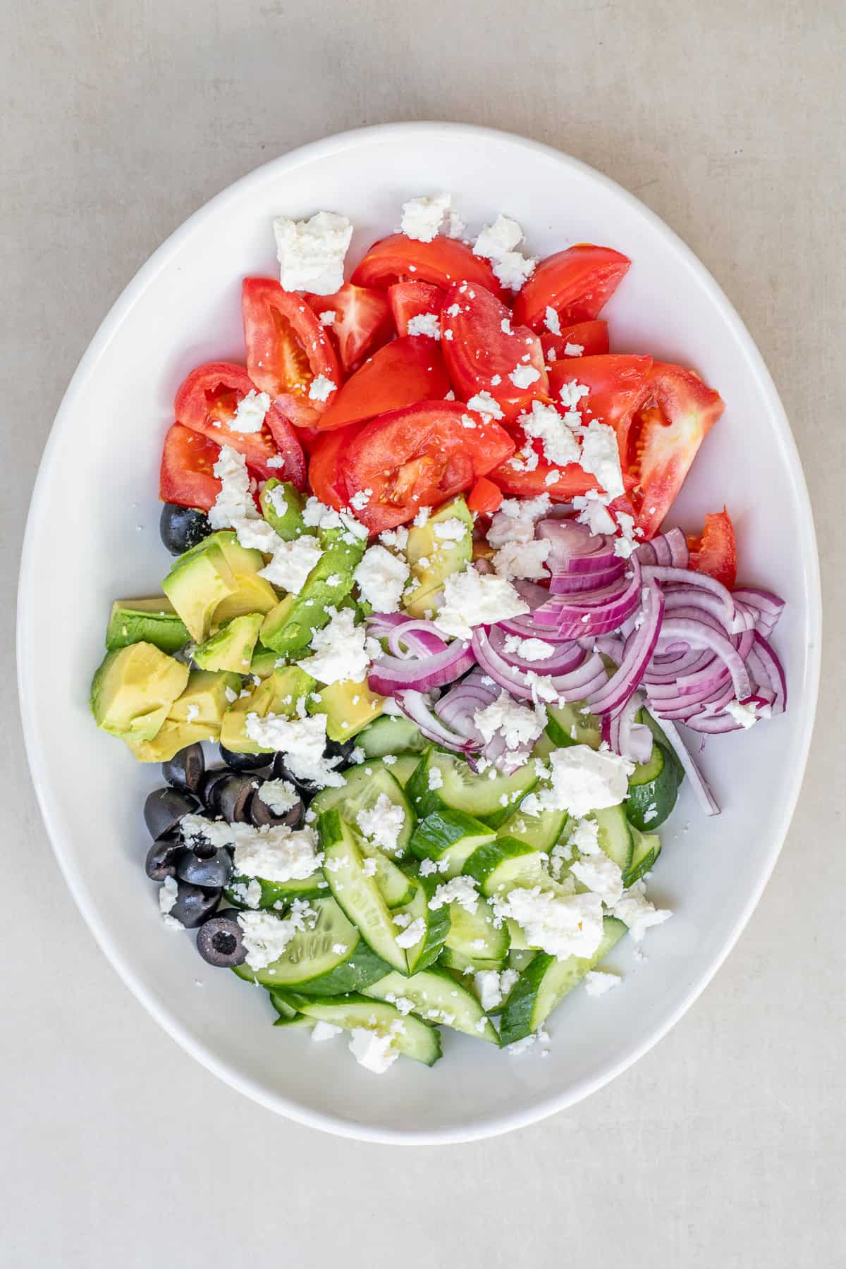 Homemade avocado Greek salad tossed with a flavorful lemon and olive oil dressing. A salad bowl with all of the salad ingredients.