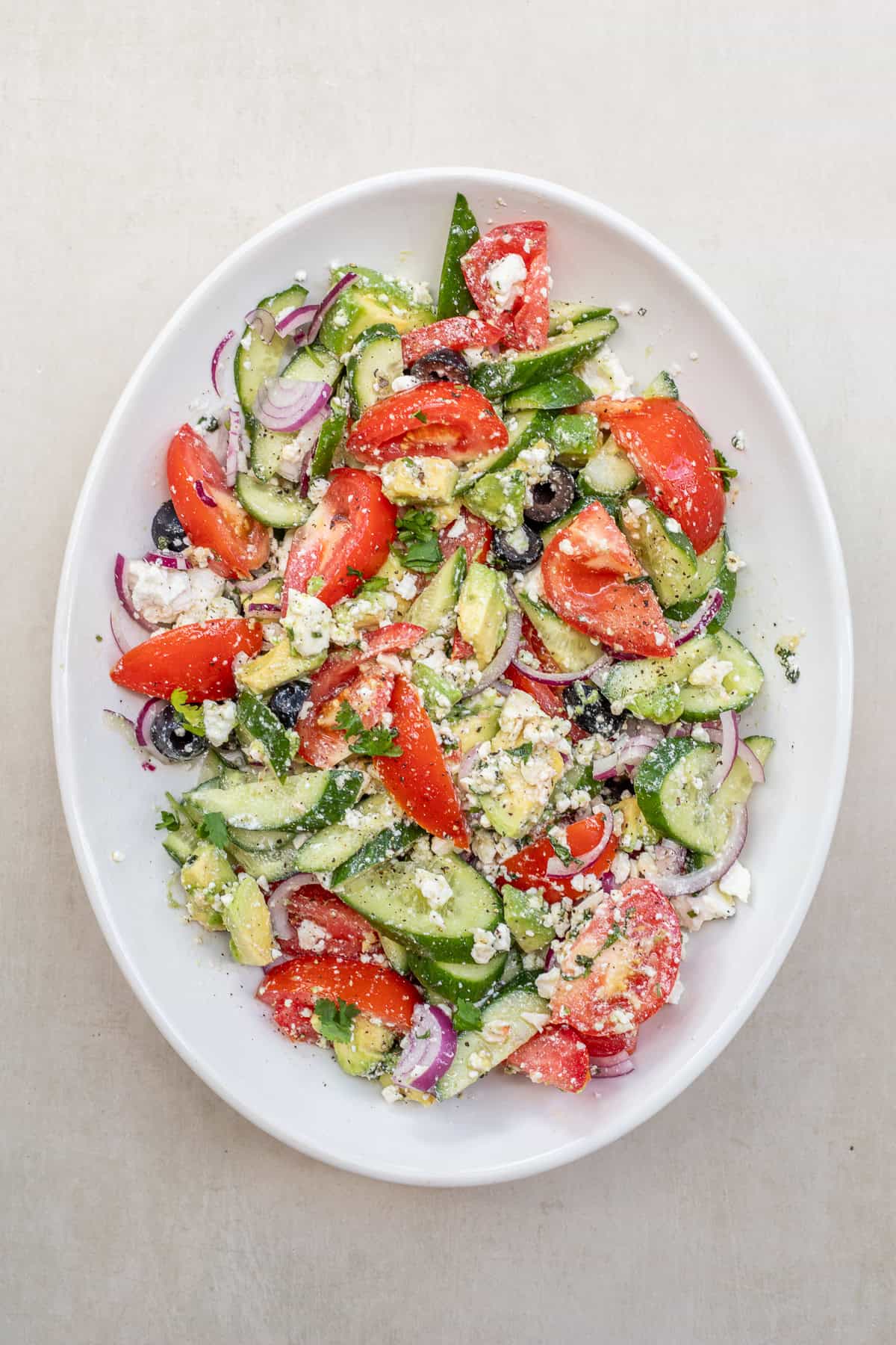 Easy Greek salad with creamy avocado, juicy tomatoes, crisp cucumbers, feta cheese, and a fresh homemade dressing. A salad bowl with the tossed greek salad.