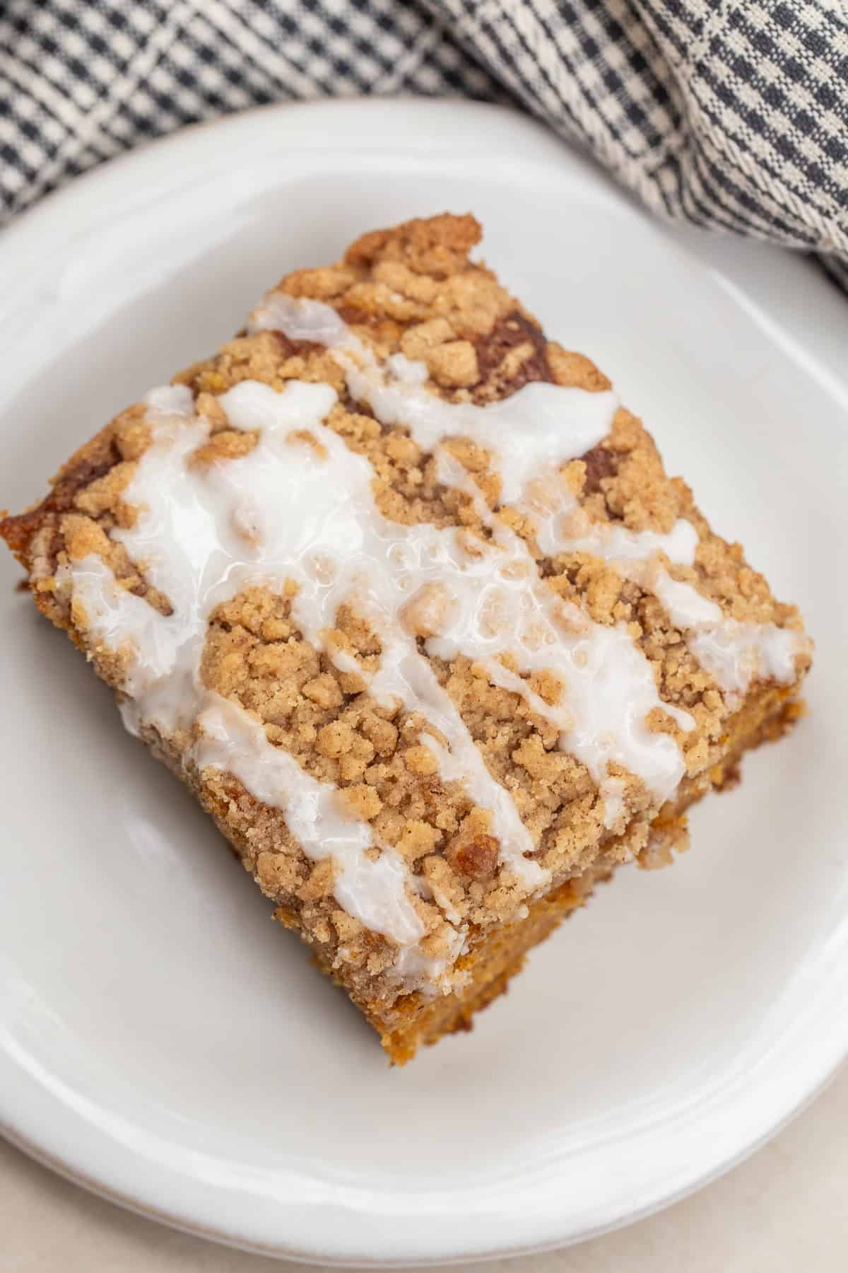 A soft and fluffy pumpkin coffee cake topped with a generous layer of buttery, spiced streusel. A plate with a slice of pumpkin coffee cake, topped with a creamy glaze.