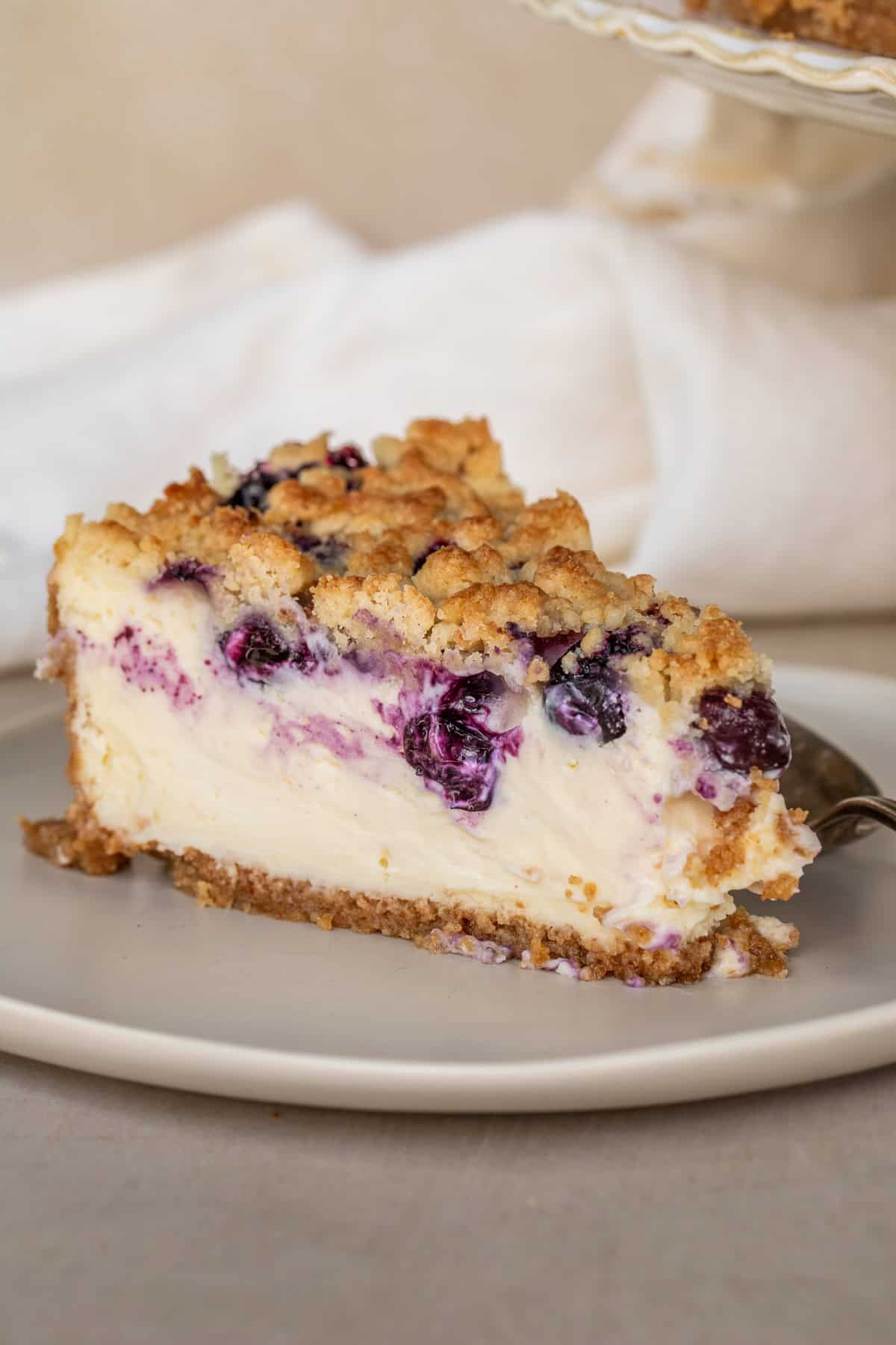 Homemade blueberry crumble cheesecake topped with sweet blueberries and golden buttery crumbs. A slice of blueberry crumble cheesecake.