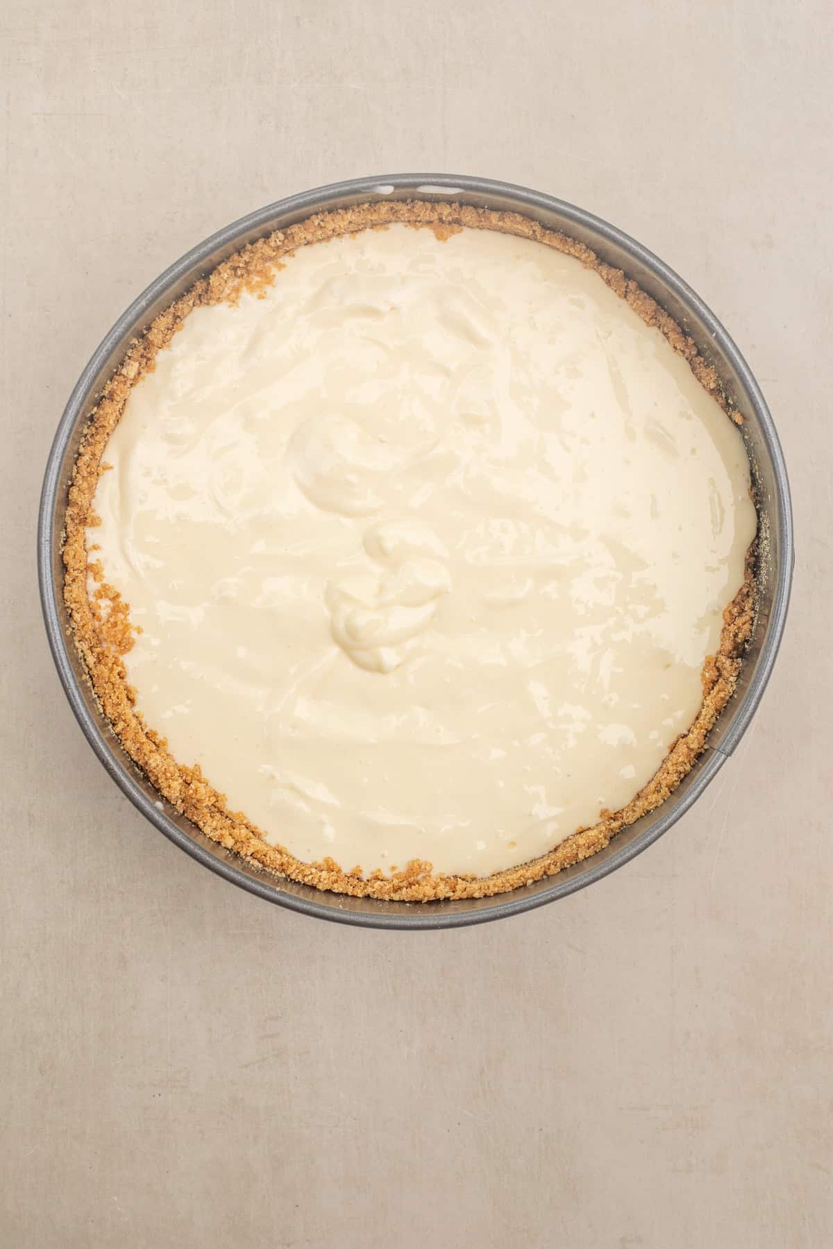 Creamy cheesecake with a sweet blueberry topping and golden brown crumble. The cake pan with the cheesecake layer over the crust.