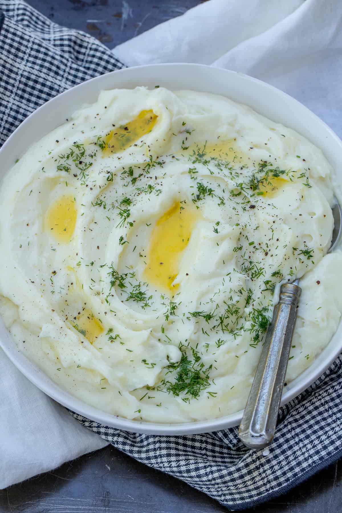 Cheesy Mashed Potatoes Recipe A bowl of cheesy mashed potatoes topped with melted butter and fresh herbs.