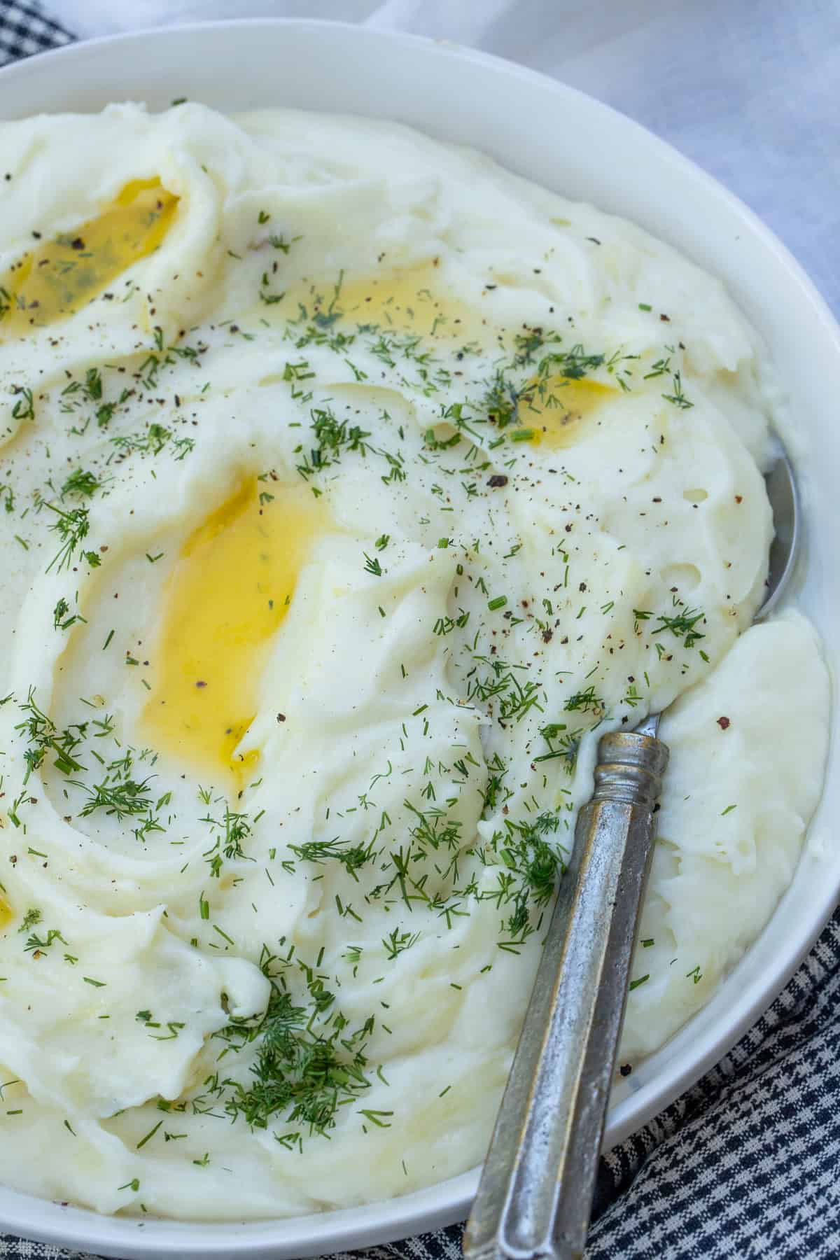 Buttery Cheesy Mashed Potatoes A bowl of cheesy potatoes topped with fresh herbs.