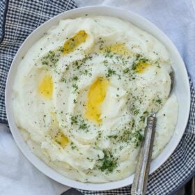 A bowl of cheesy mashed potatoes with butter and chives.